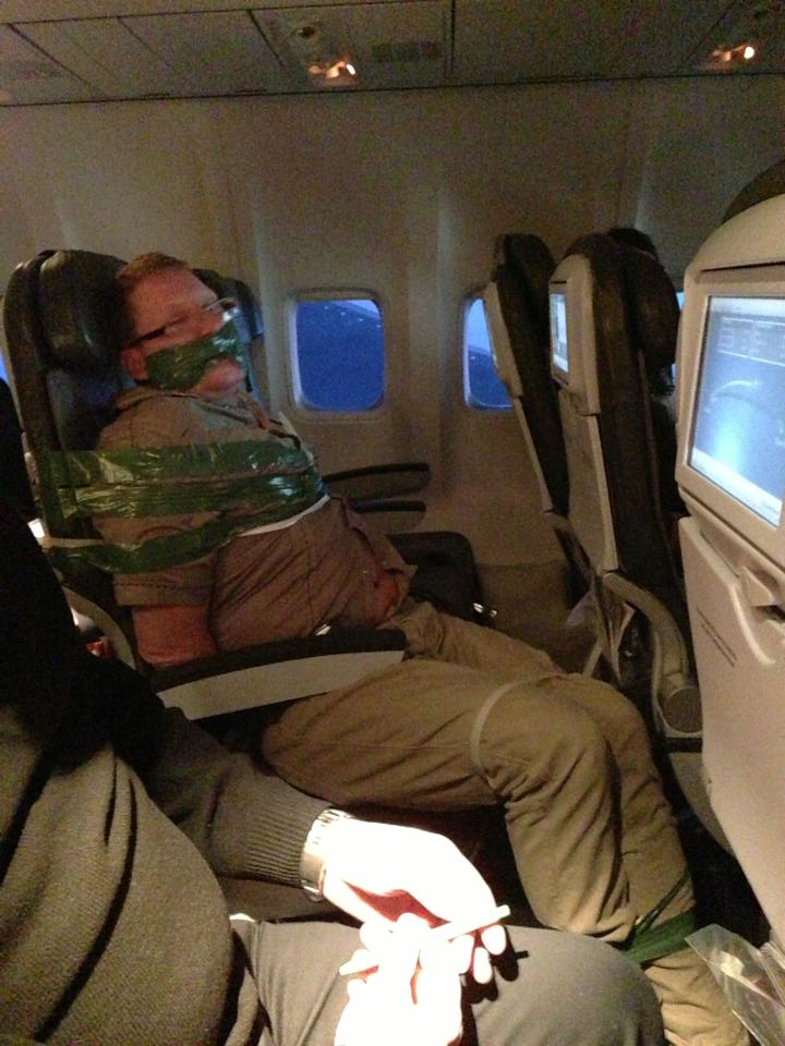 A man is taped to an airplane seat with green tape.